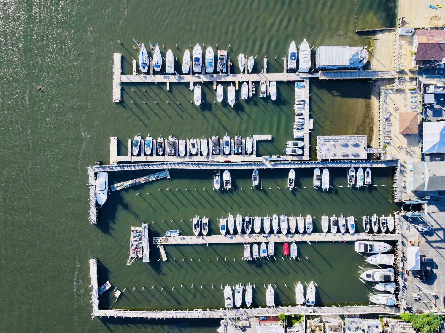 Top-down aerial photograph of a Highlands marina, rows of boats in slips along the docks with a road and buildings at the edge, 2026