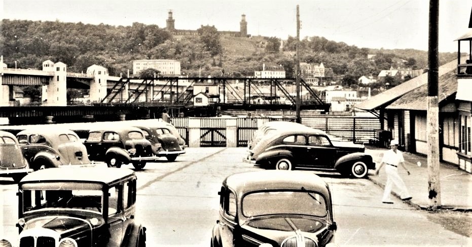 The Sandlass Beach Club parking lot ca. 1940 — prewar sedans in the lot, Twin Lights on the Highlands ridge behind, the Route 36 high bridge to their left, the old ferry-pier bridge partially visible