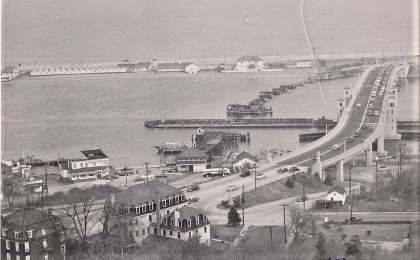 An elevated view of Highlands waterfront ca. 1950 — Bay Avenue in the foreground with docks and cottages, the Route 36 bridge climbing at right, the Sandlass Beach Club bathhouses on the peninsula behind