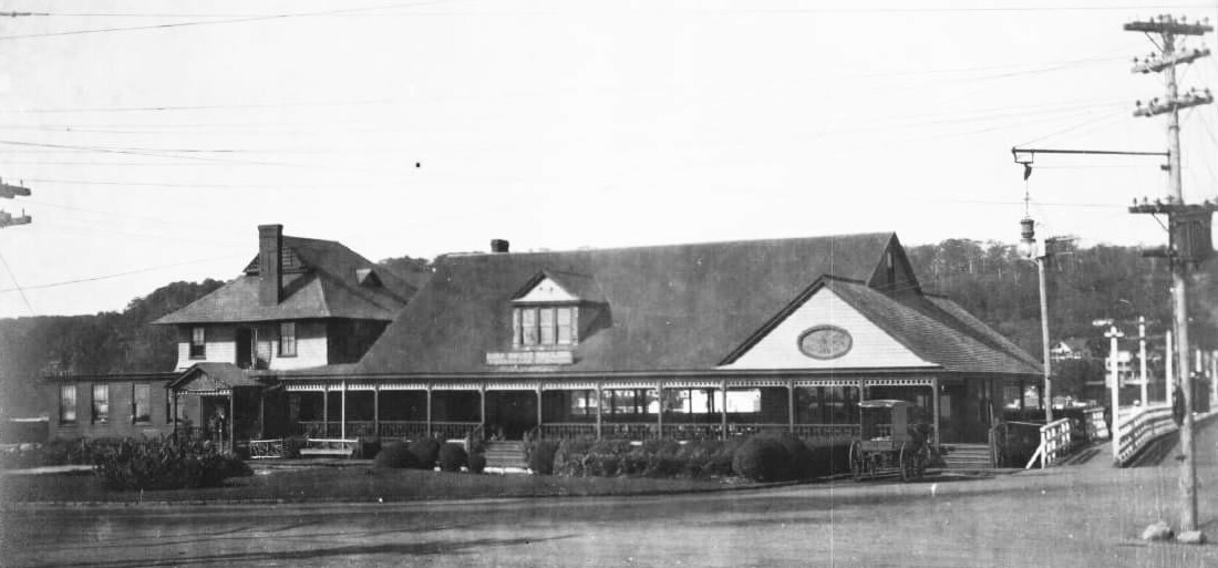The Sandlass Beach Club at Highland Beach ca. 1908 — a long low wooden pavilion with a covered veranda across its full seaward face, a horse-drawn wagon at right, the wagon bridge to the mainland at far right