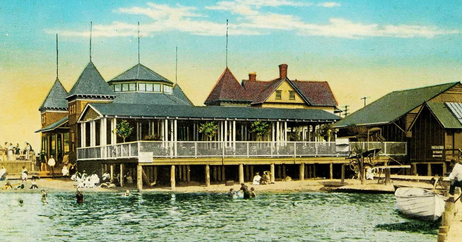 A hand-colored postcard ca. 1908 of the Sandlass Pavilion at low tide — the pavilion supported on wooden pilings with a wide covered veranda, the Bamboo Room dance-hall building beside it, a rowboat moored at the corner