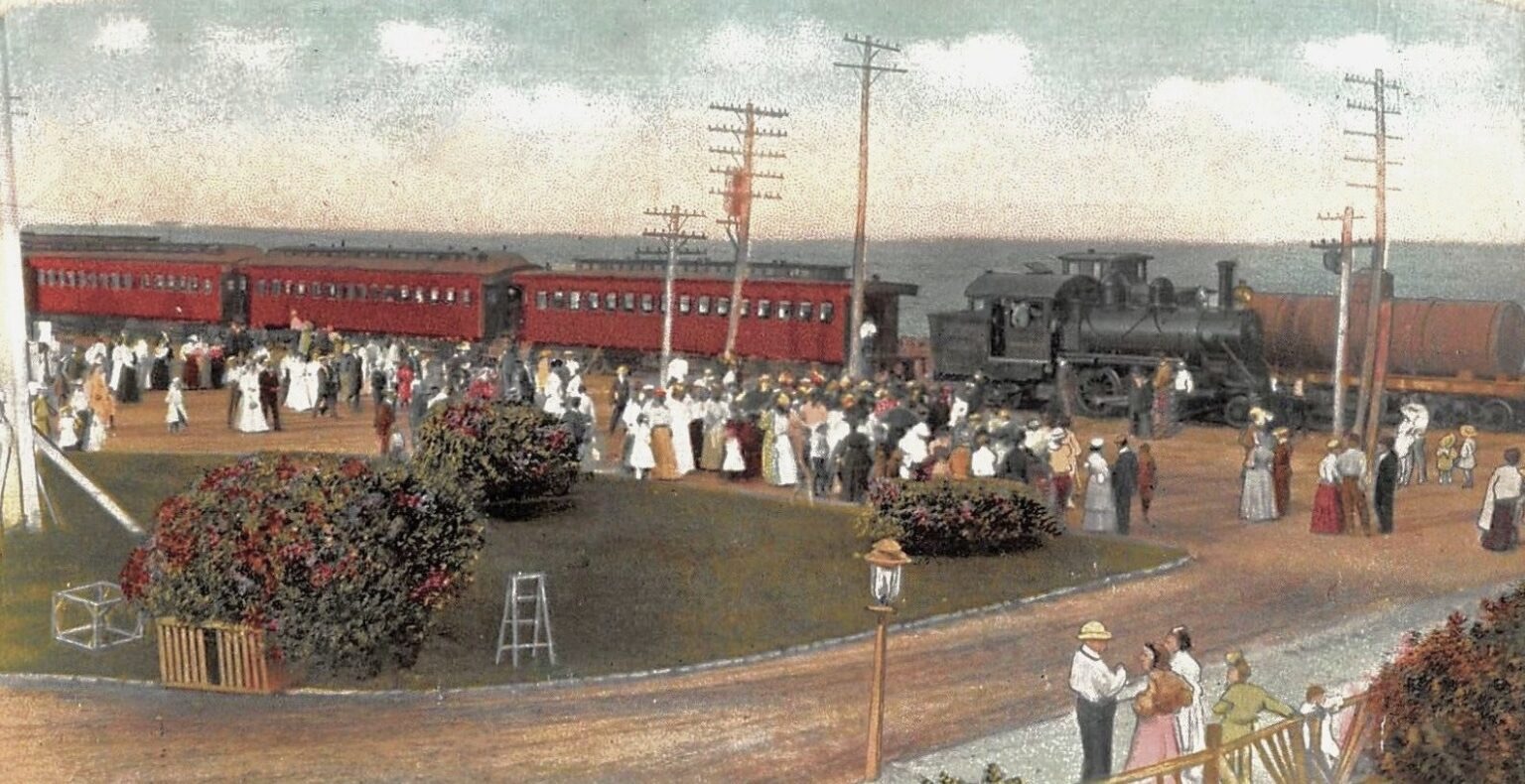 A hand-colored postcard ca. 1908 of a New Jersey Southern train arriving at Highland Beach — a maroon five-car consist behind a small 4-4-0 steam locomotive, a crowd of Edwardian passengers on the platform, ornamental flower beds