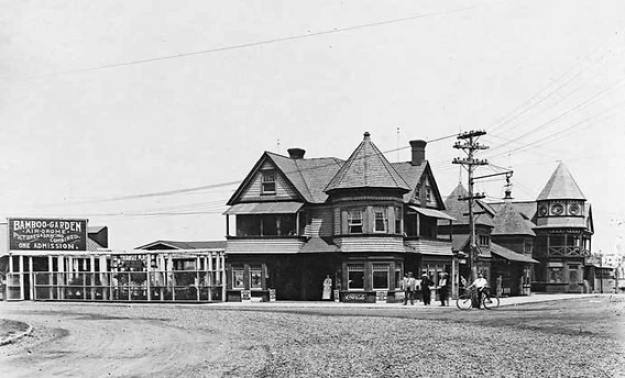 A sepia photograph ca. 1912 of the Sandlass entertainment complex at Highland Beach from across the road — Victorian gingerbread pavilion office with hexagonal corner tower, BAMBOO-GARDEN AIR-DROME signboard at far left, a man on a bicycle at the corner