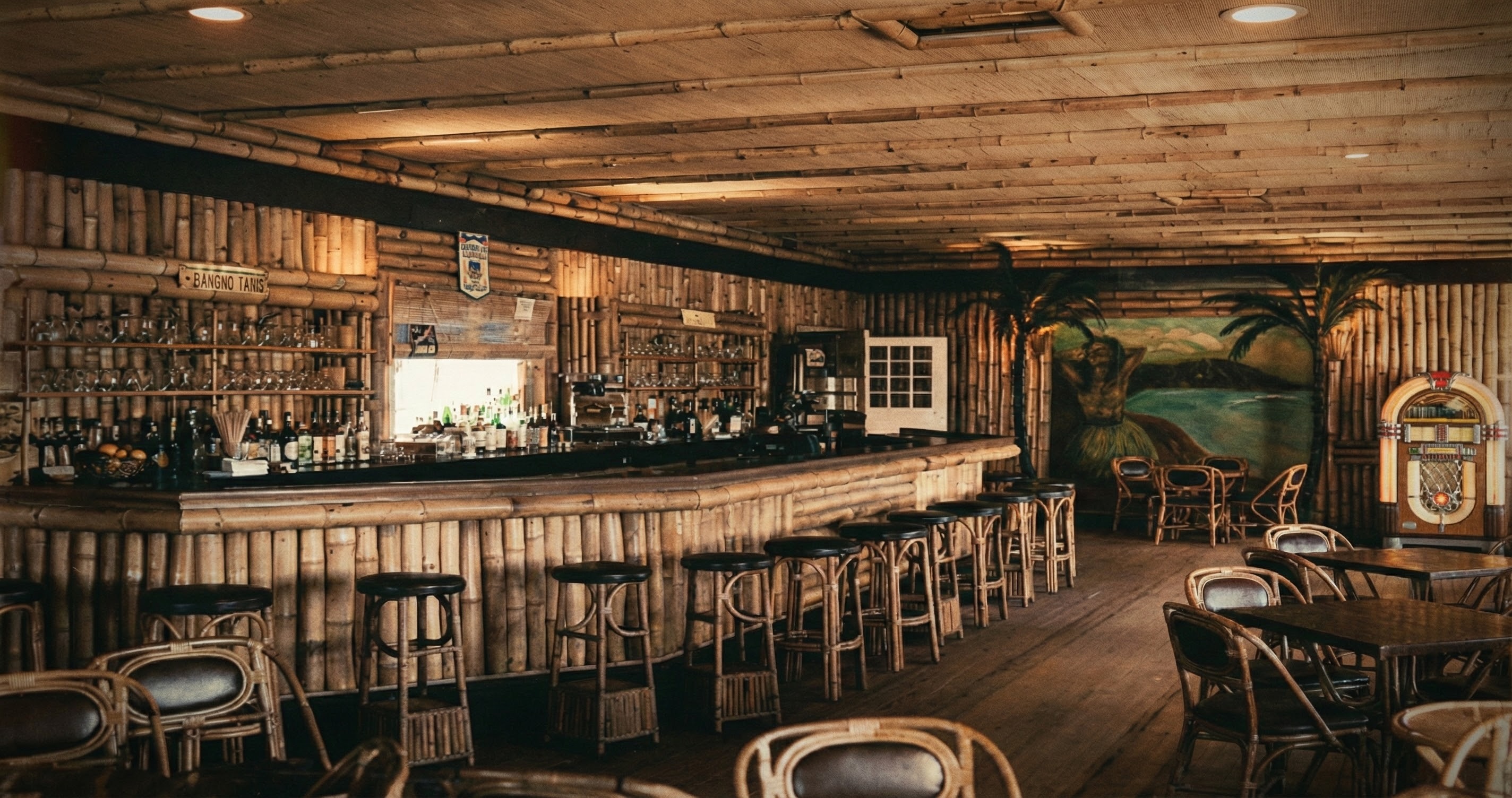 A high-resolution color interior photograph ca. 1948 of the Bamboo Room bar at Highland Beach — a curved bamboo-clad bar with Bentwood stools, glassware and bottles on bamboo shelves under a bamboo-battened ceiling, a Hawaiian-dancer mural with palm trees on the far wall, a Wurlitzer jukebox at right
