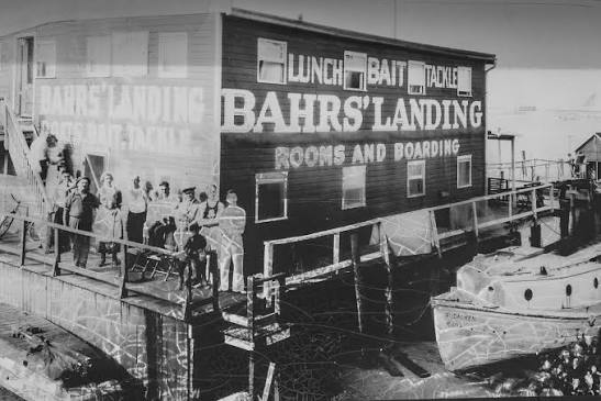 An early photograph of Bahrs' Landing — the houseboat's dockside wall lettered LUNCH · BAIT · TACKLE and BAHRS' LANDING · ROOMS AND BOARDING, a group posed on the dock alongside it, a small boat moored in the foreground.